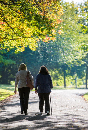 Two females, one with a walking stick walking on tree lined path.