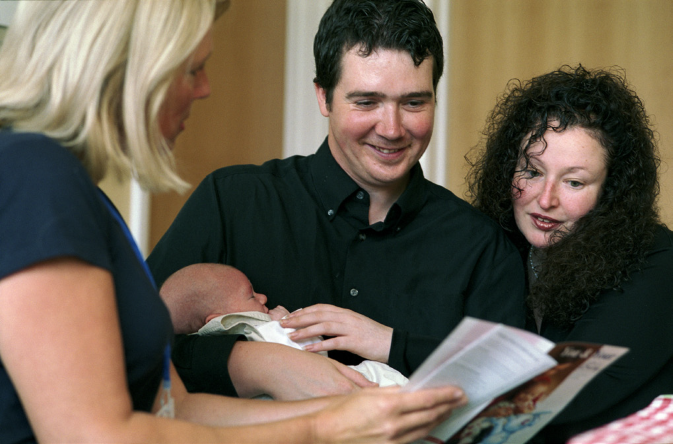 Photo of new parents and baby talking to a health visitor