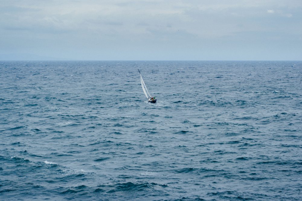 Photo of a small sailing boat in the middle of expanse of water.