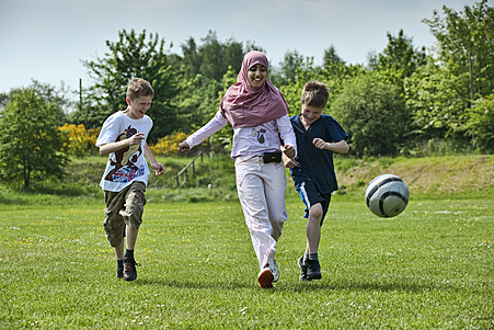 Three kids running on grass while playing with a football.