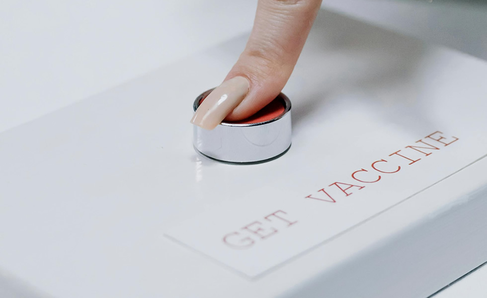 Female finger pressing a red button marked "Get Vaccine"