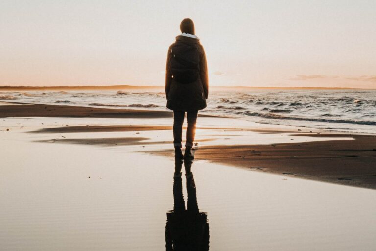 A silhouette of a person on a wet beach looking out towards the horizon