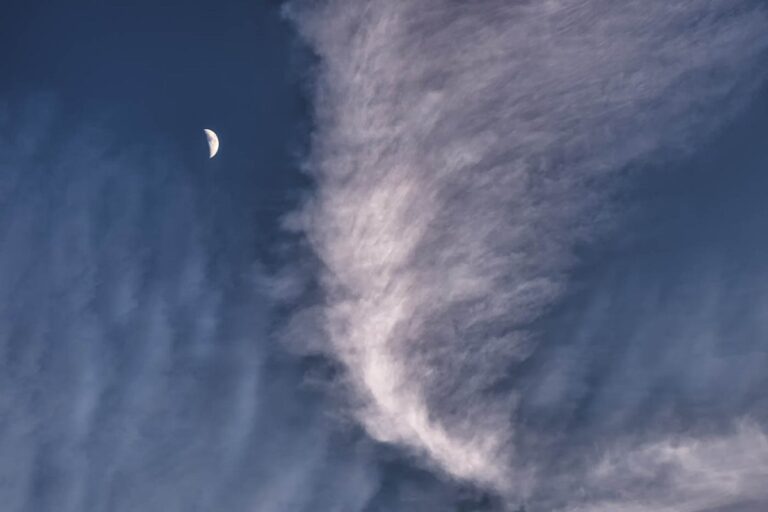 Clouds in an early evening sky with the moon appearing high on the left