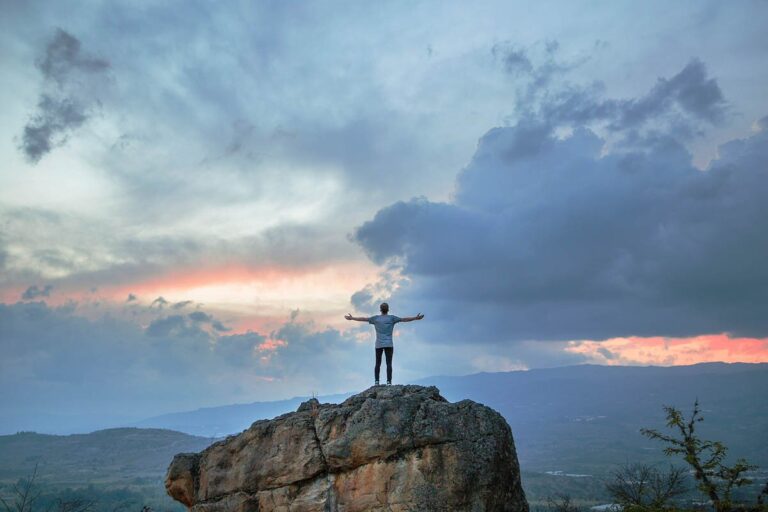 A man standing on top of a mountain looking towards an evening sky