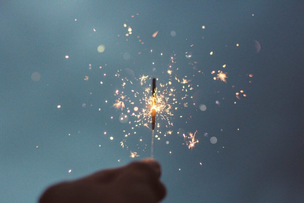 A hand holding up a lit sparkler (firework) against the night sky