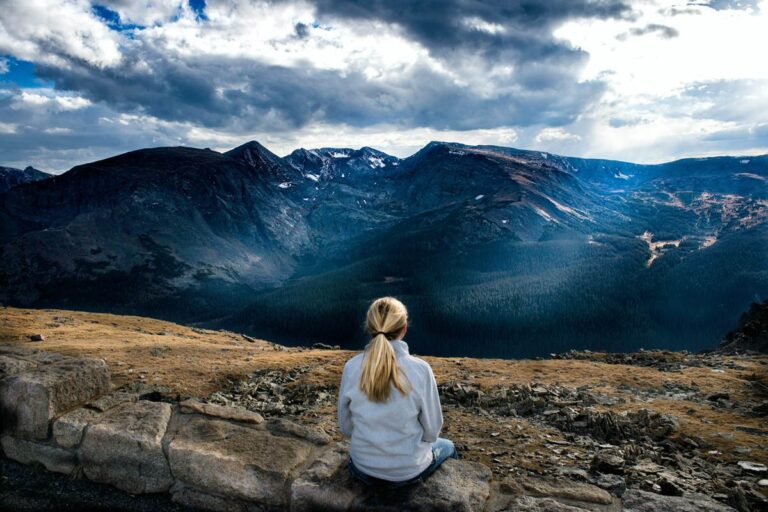 A young female sitting up a mountain looking out towards the sky