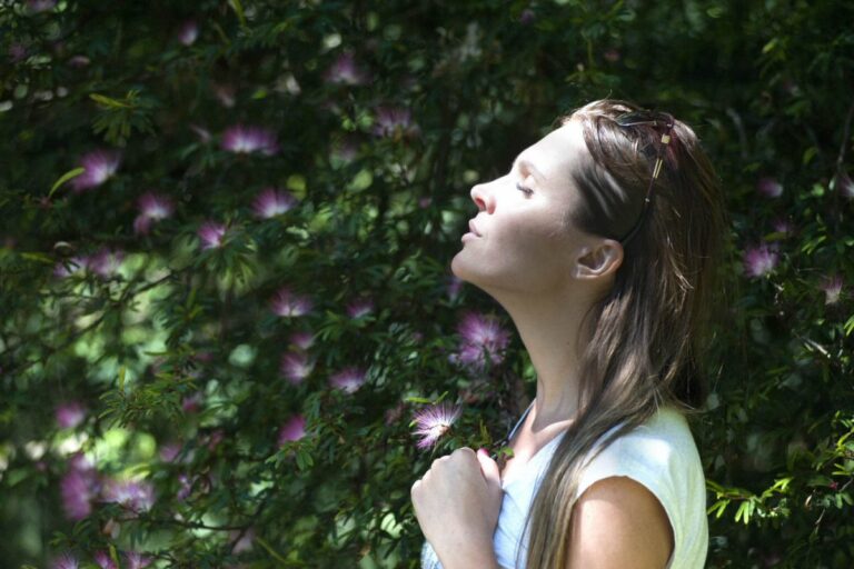 A female with eyes closed in a garden setting feeling the sun on her face